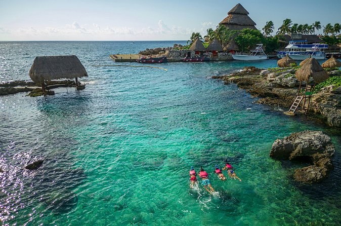 A thatched pavilion standing out over a turquoise cove, swimmers below it