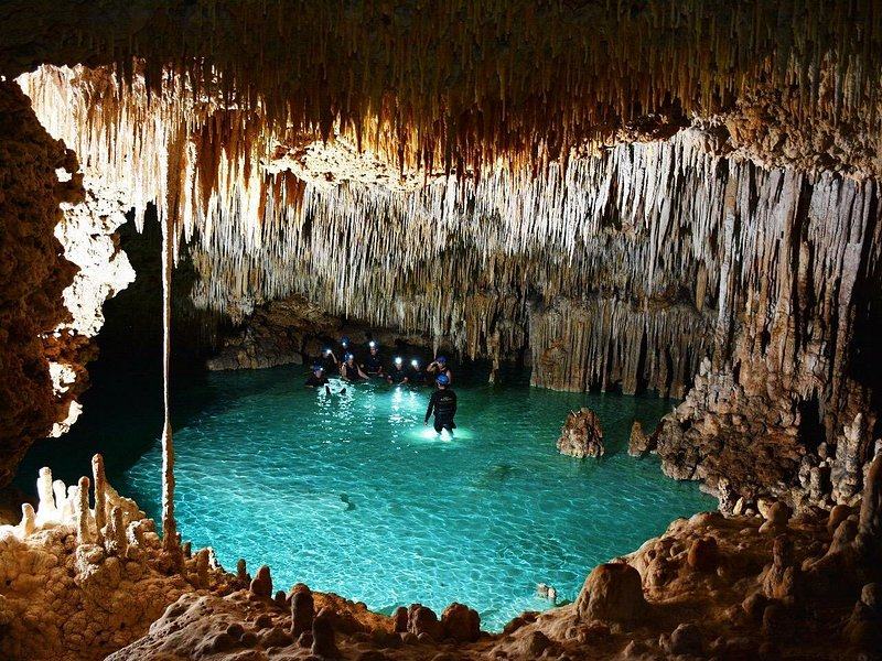 A lit blue pool under a low roof of stalactites