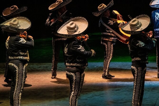 Four musicians in wide hats and braided suits, lit from behind on a dark stage