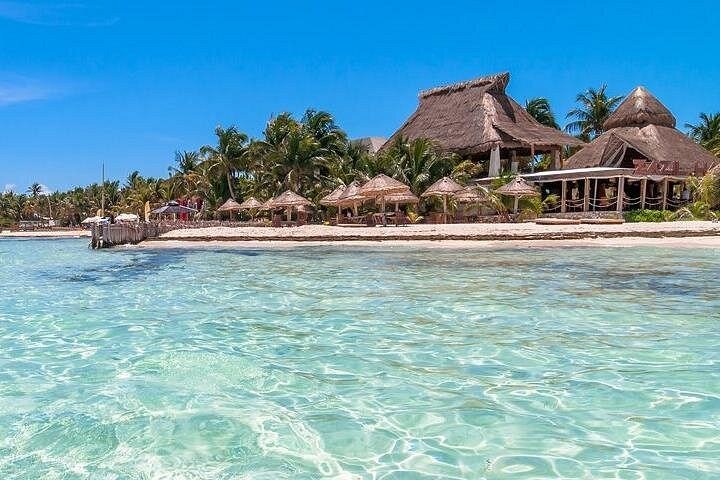 Thatched palapas along a white beach above clear, shallow water