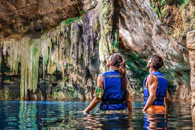 Two swimmers in life jackets, seen from behind, in a chamber hung with stalactites