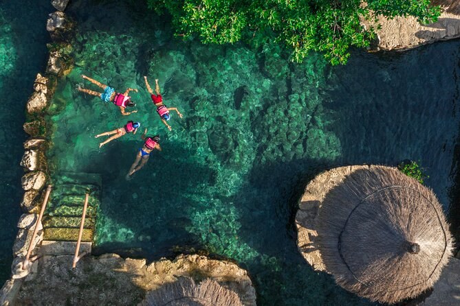 Looking straight down on swimmers in life jackets crossing a deep green pool