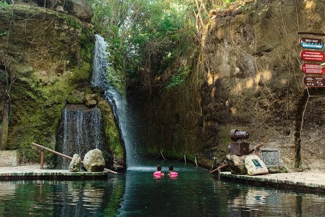 A waterfall dropping down a pale rock wall into a still green pool