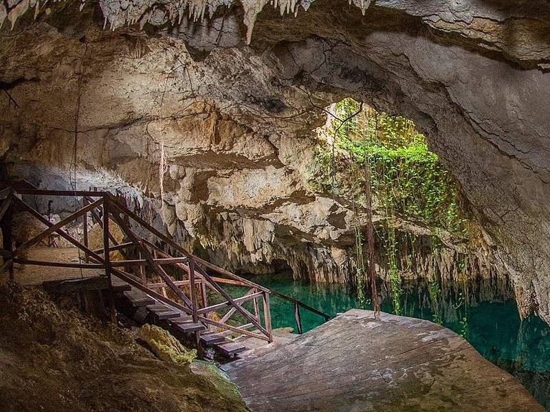 A wooden stair running down into a cave above green water